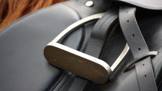 A close-up photograph of a black leather saddle and silver metal stirrup.